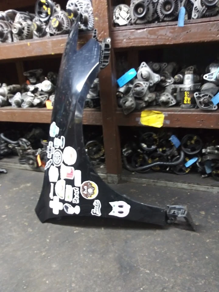 Black auto part covered in stickers on a shelf.