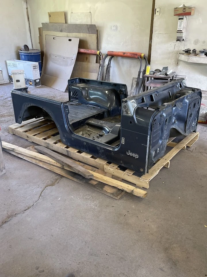 Jeep body shell on a wooden pallet in a workshop.