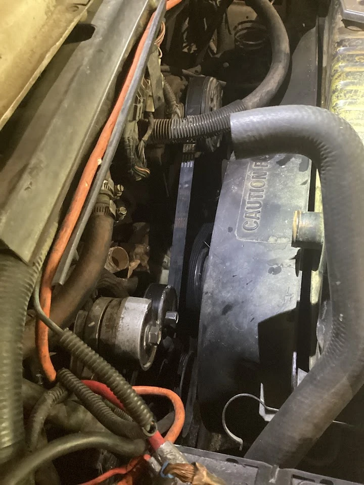 Engine compartment with belts and wires visible.