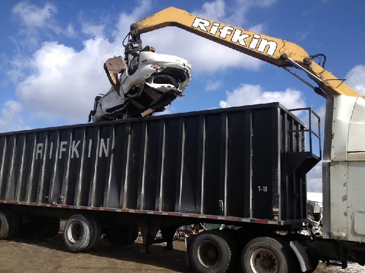 Lifting a crushed car into a scrapyard container.