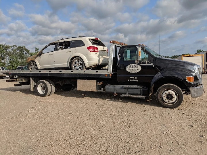 Tow truck transporting a white vehicle on flatbed.