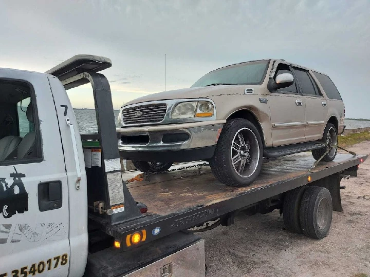 Towing service with a junk SUV on a flatbed truck.