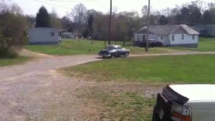 Old car passing through a gravel road in a rural area.