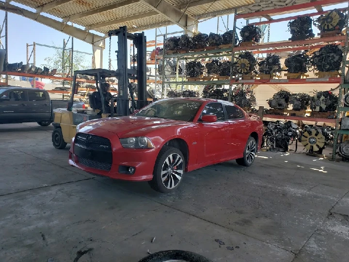 Red car in a wrecking yard with engines in background.