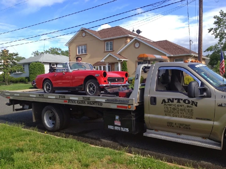 Red vintage car on tow truck outside a home.