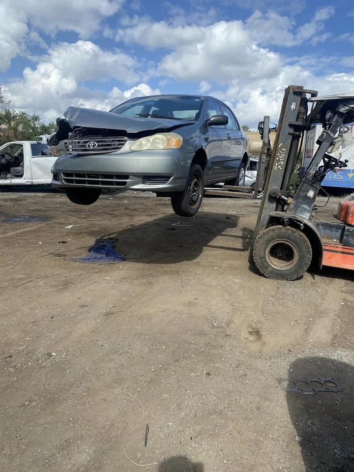 A forklift lifting a damaged silver car.