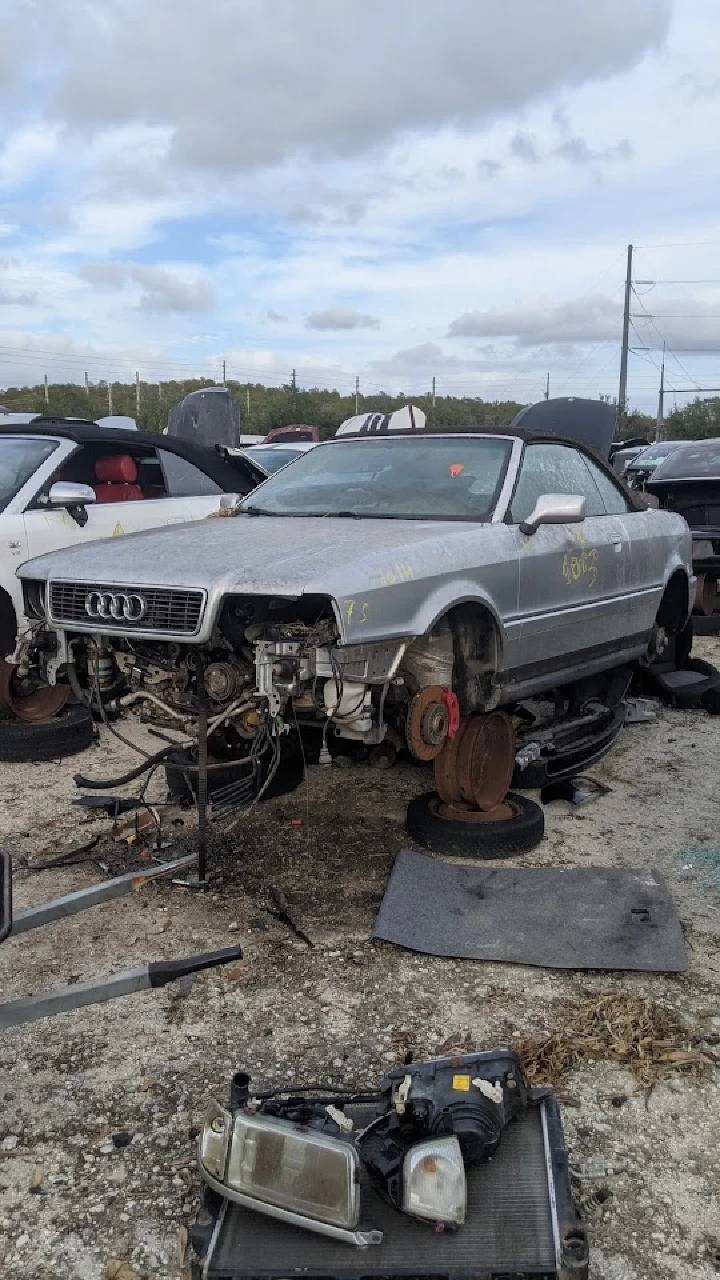 Abandoned Audi with missing parts in a junkyard.