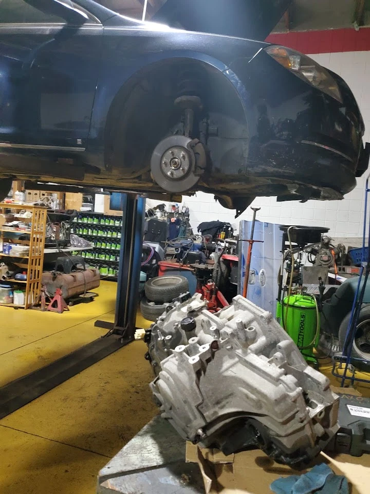 Car on lift with engine part in a workshop setting.