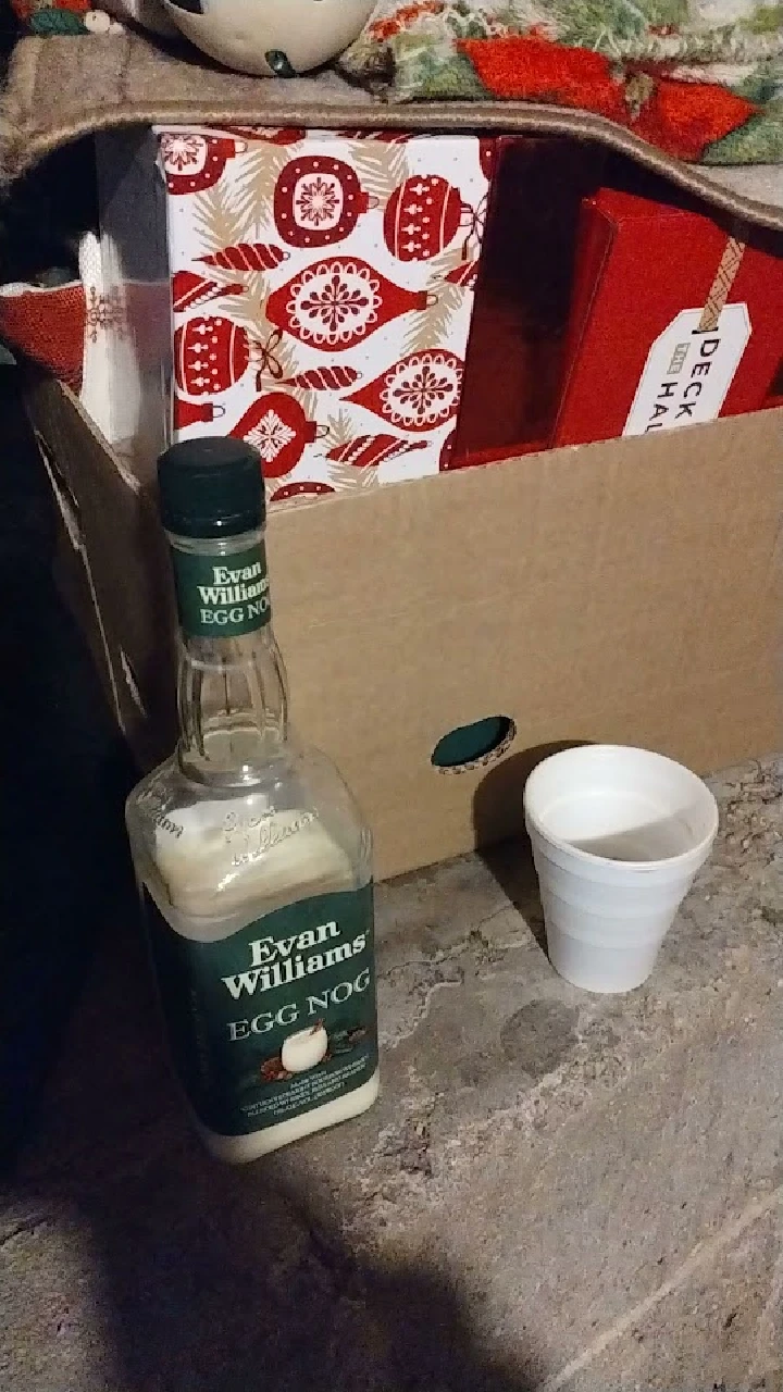 Eggnog bottle beside a white cup and gifts.