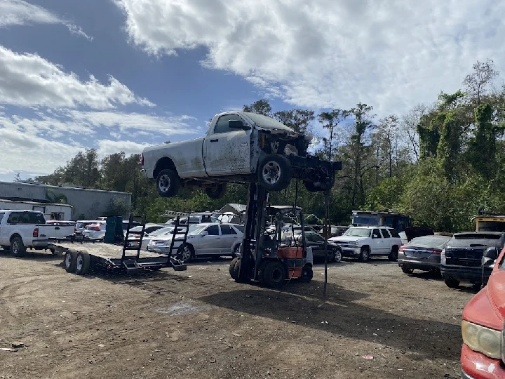 Forklift lifting an old truck in a junkyard.