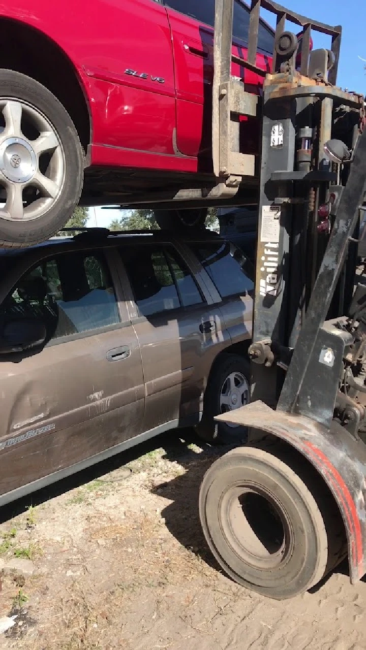 Forklift lifting a red car over a brown vehicle.