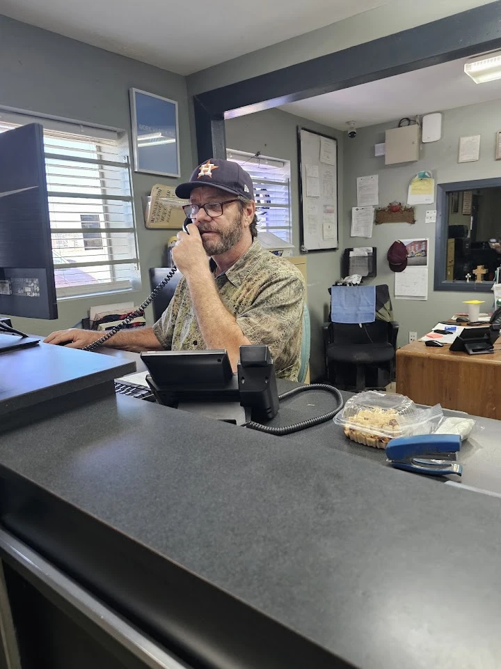 Man at desk answering phone in junkyard office.