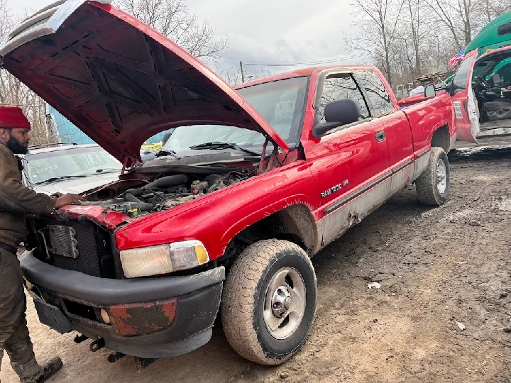 Red pickup truck with hood raised, in a salvage yard.