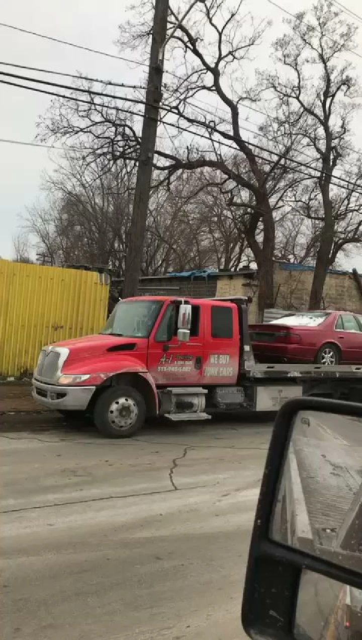 Red towing truck with a junk car on the flatbed.