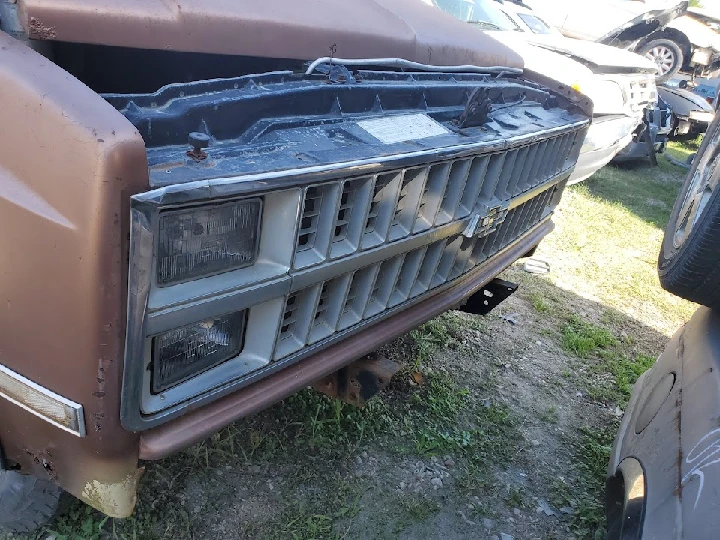 Rusty car front with headlights, in a junkyard.