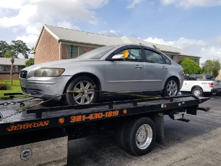 Silver car being towed on a flatbed truck.