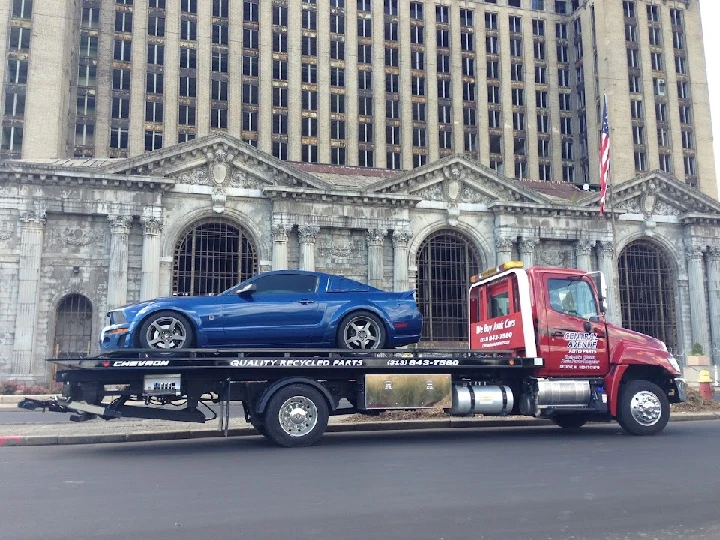 Tow truck with a blue car in front of a building.