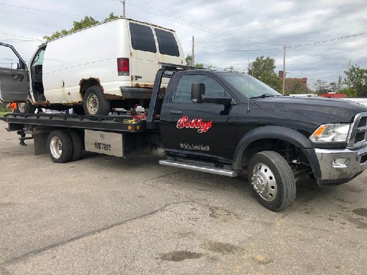 Tow truck carrying an old van for junk removal.