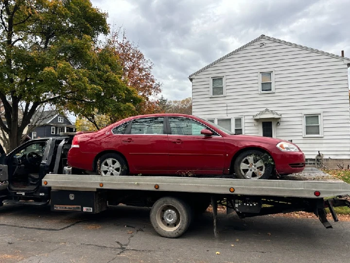 Tow truck carrying a red car in front of a house.