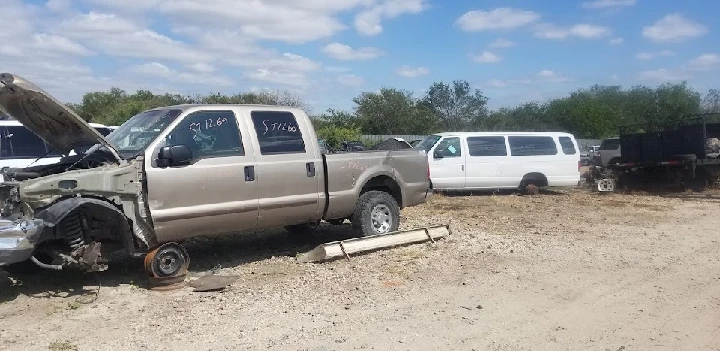 Trucks and vans in a salvage yard under a blue sky.