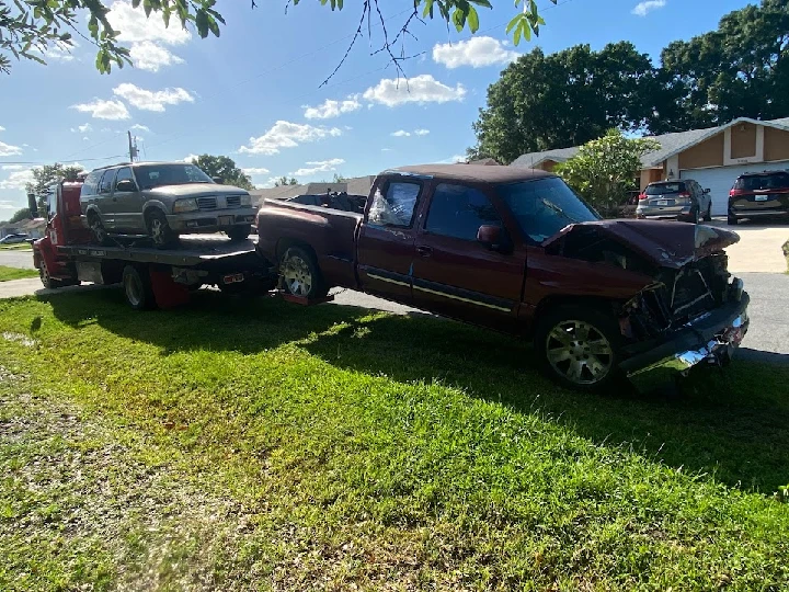 Two junk cars on a tow truck in a grassy area.