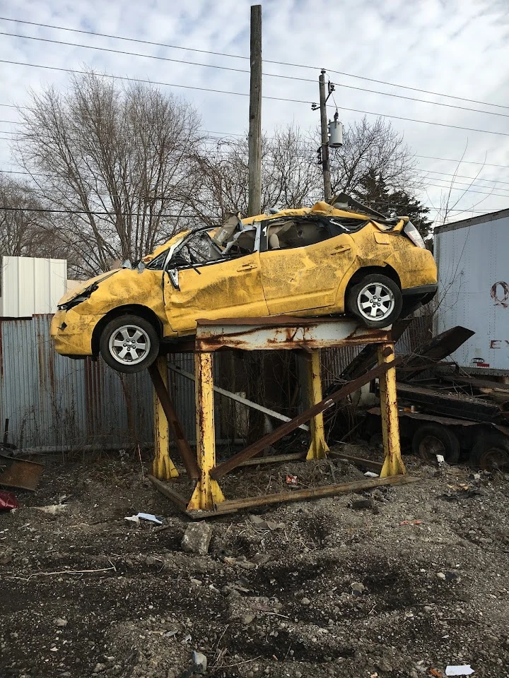 Wrecked yellow car on a platform in a junkyard.