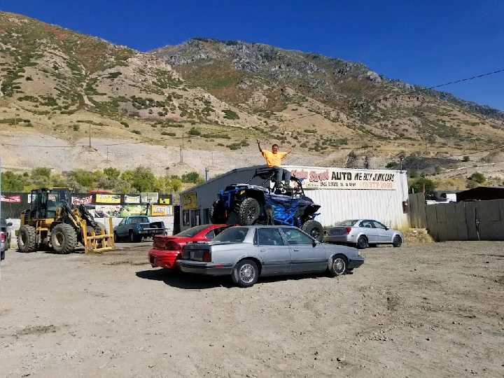 A man on an ATV atop stacked junk cars.