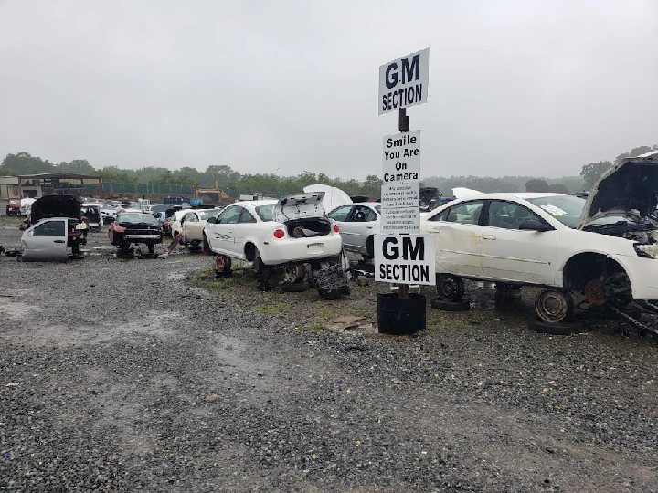 Abandoned cars in a junkyard under cloudy skies.