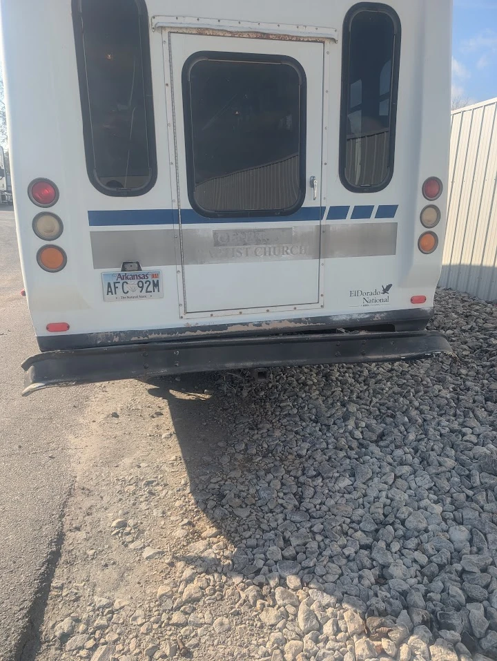 Back view of a bus parked on gravel.