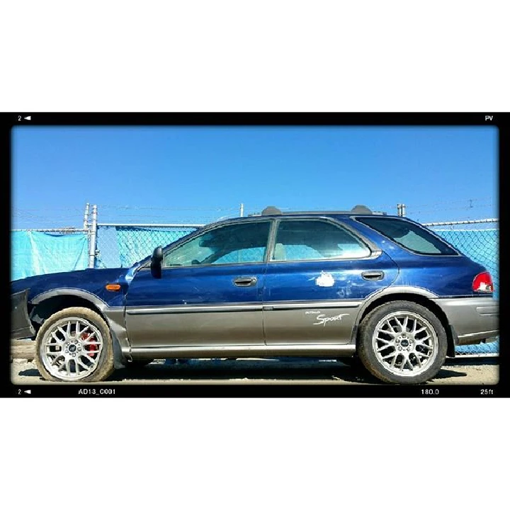 Blue car parked, surrounded by a chain link fence.