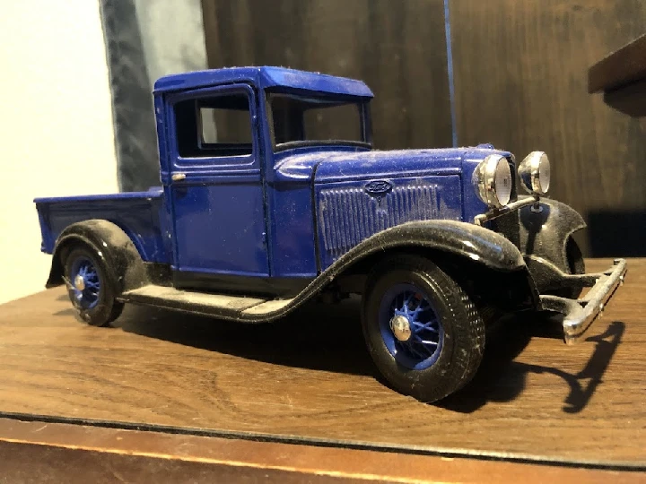 Blue vintage pickup truck model on a wooden surface.