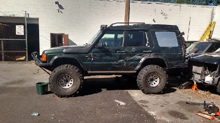 Damaged green SUV in a vehicle junkyard.