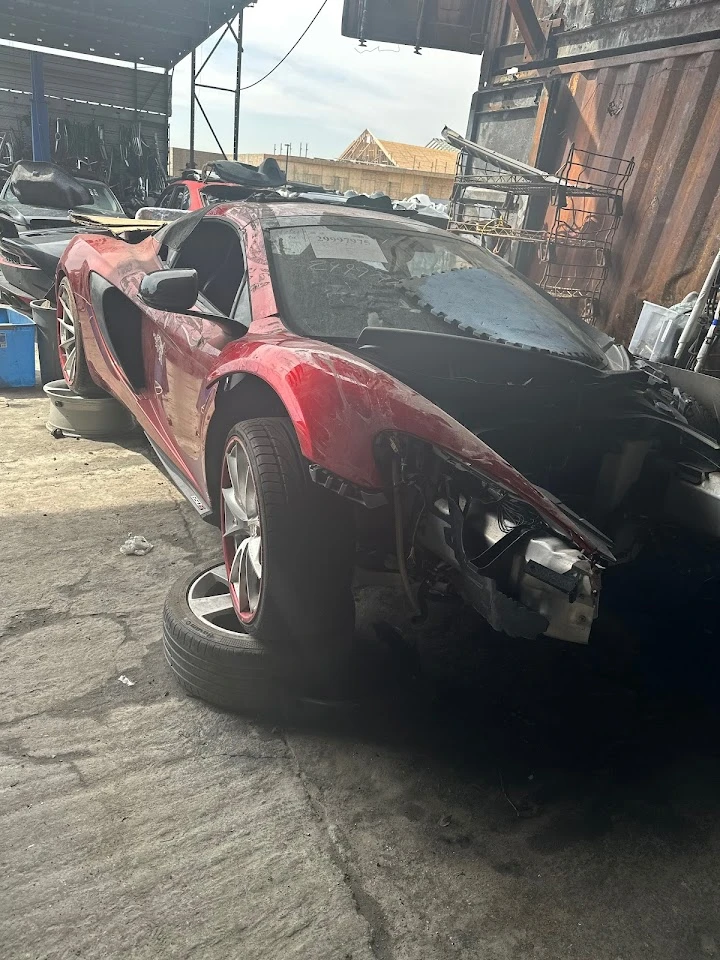 Damaged red sports car at an auto salvage yard.