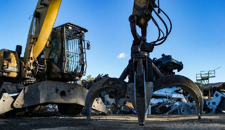 Excavator grappling metal debris at recycling site.