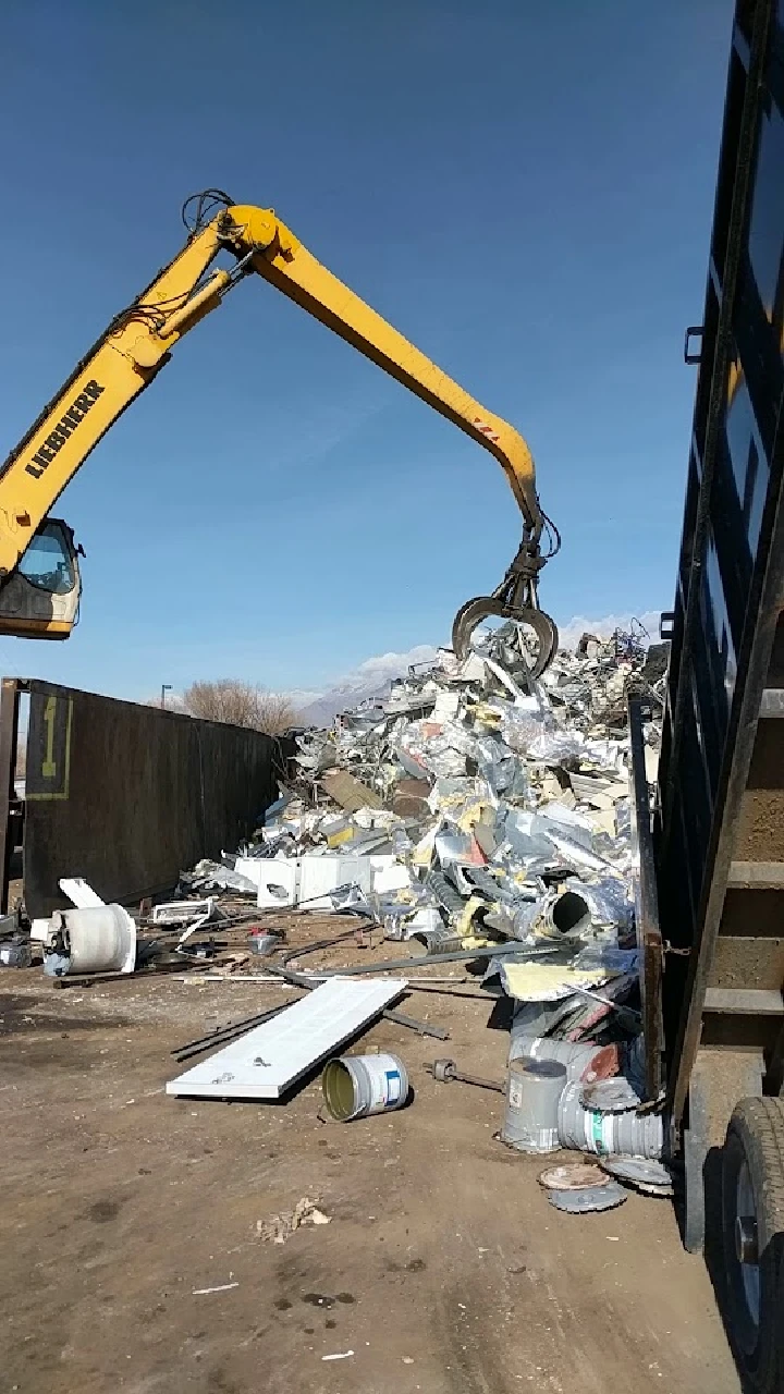 Excavator lifting scrap metal at a recycling site.