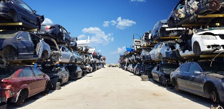 Junkyard filled with stacked, old cars under blue sky.