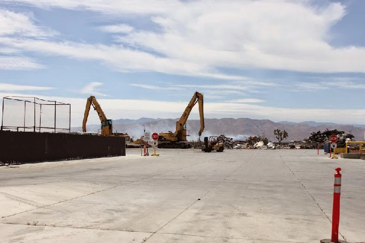 Recycling yard with heavy machinery and mountains.