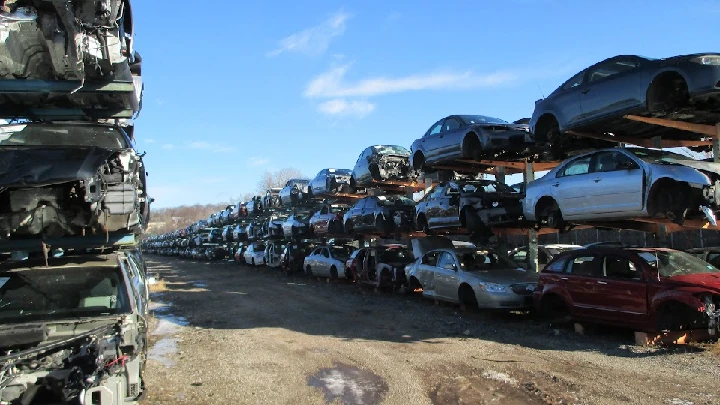 Stacked cars in a junkyard under a blue sky.