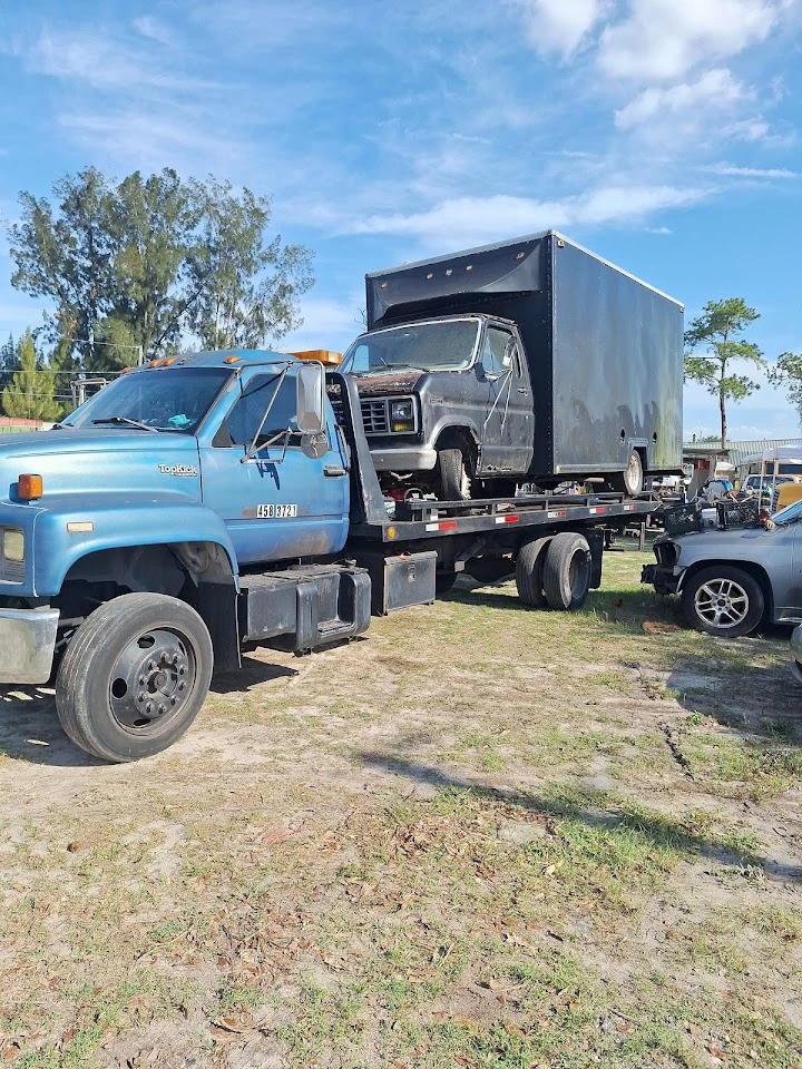 Tow truck carrying two junk vehicles in a yard.