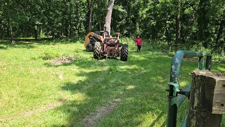 Tractor in a wooded area with a person nearby.