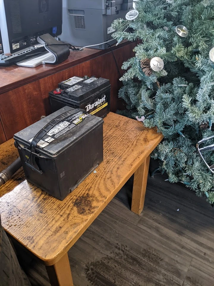 Two car batteries on a wooden table beside a tree.