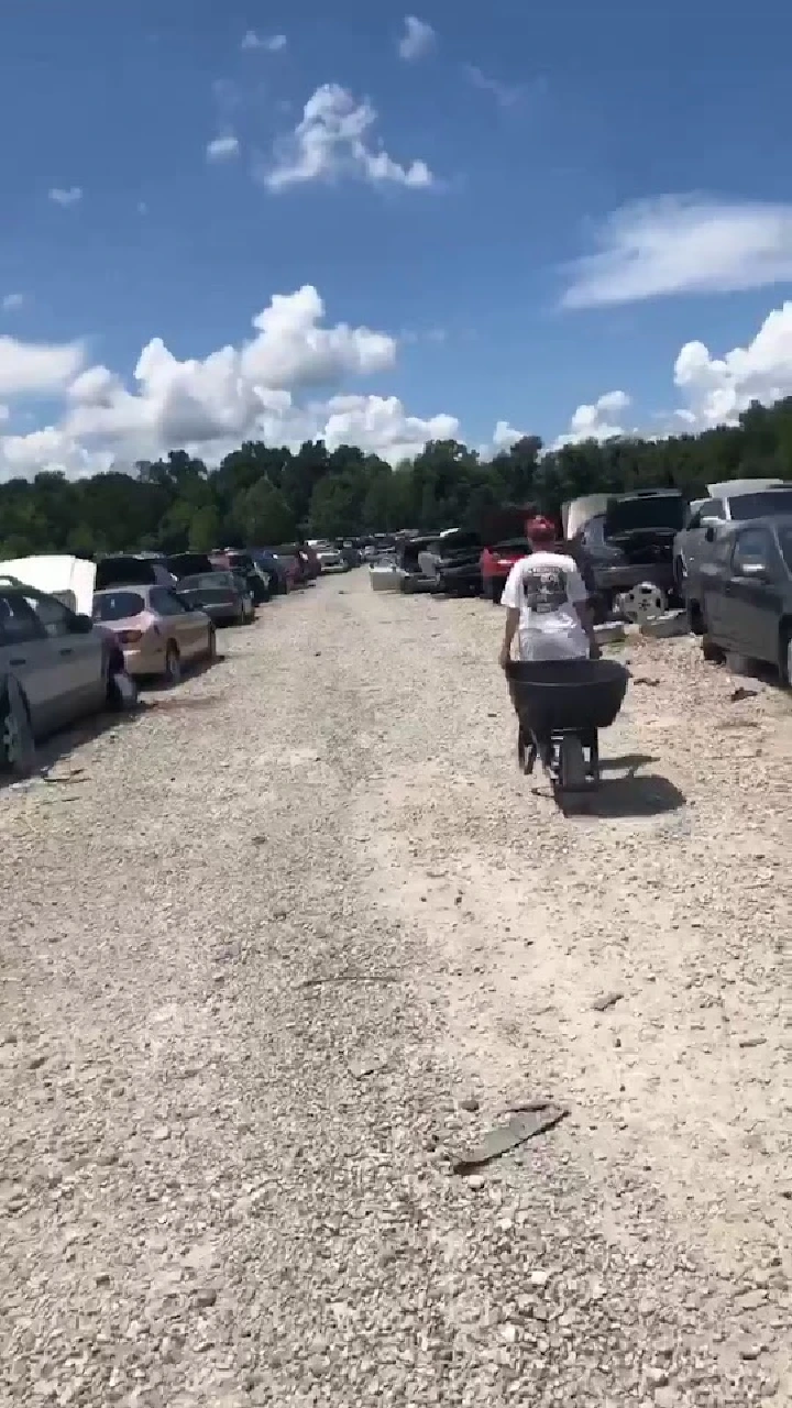 A person pushes a wheelbarrow in a junkyard.