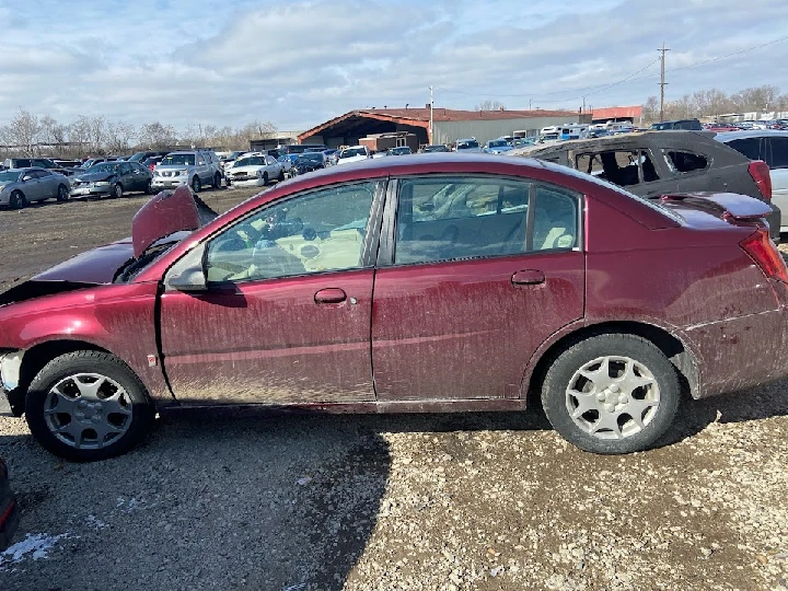 Abandoned red sedan in a junkyard setting.