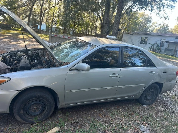 Abandoned silver car with open hood outdoors.