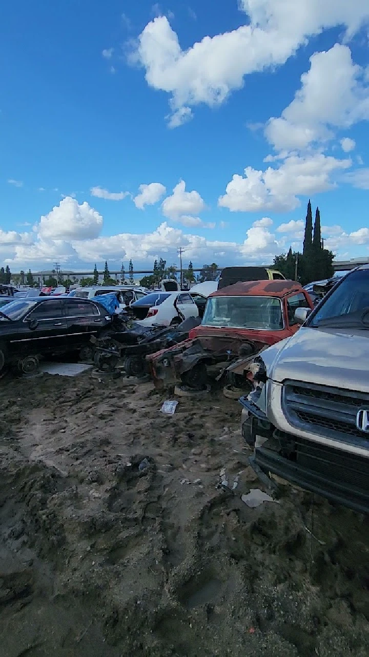 Abandoned vehicles in a salvage yard under blue skies.