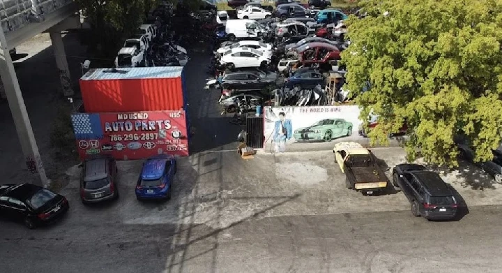 Auto parts yard with diverse vehicles and signage.