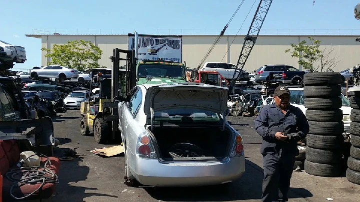 Auto wrecking yard with silver car and worker.