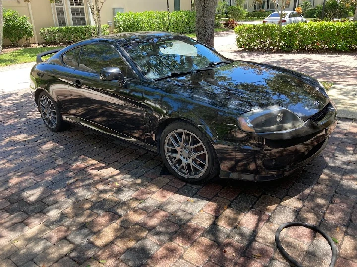 Black sports coupe parked on a brick driveway.