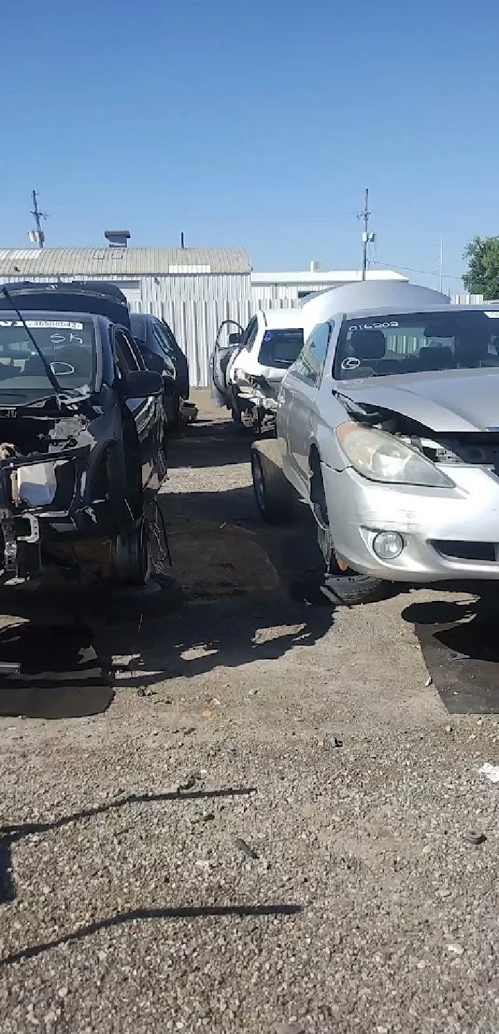 Cars in a salvage yard under a clear blue sky.