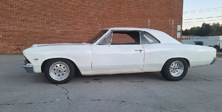 Classic white car parked beside a brick wall.